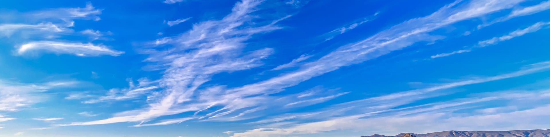 Un paisaje panorámico con colinas ondulantes, cielo azul despejado y montañas lejanas.