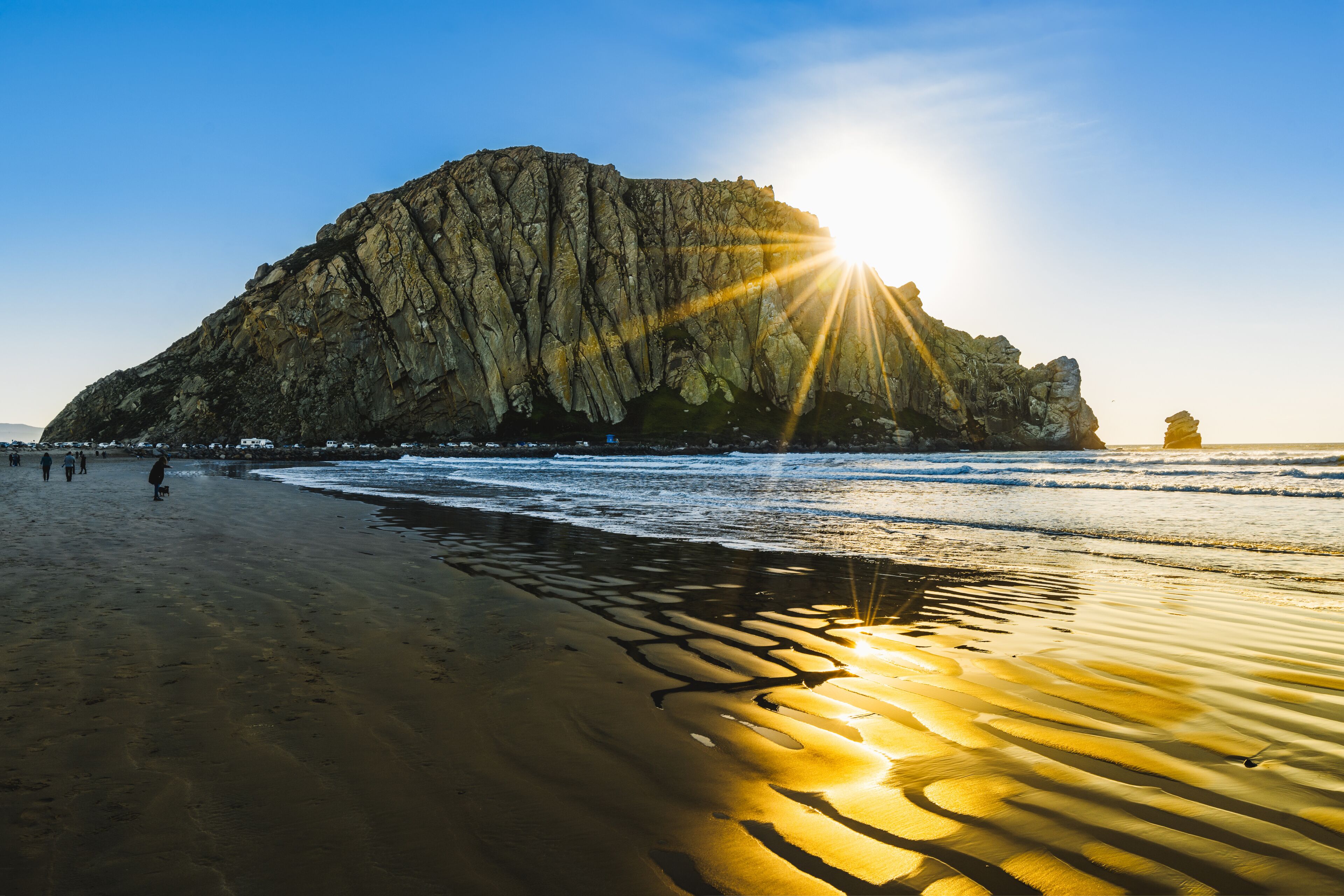 A rocky cliff by the sea with the sun shining on the sand.