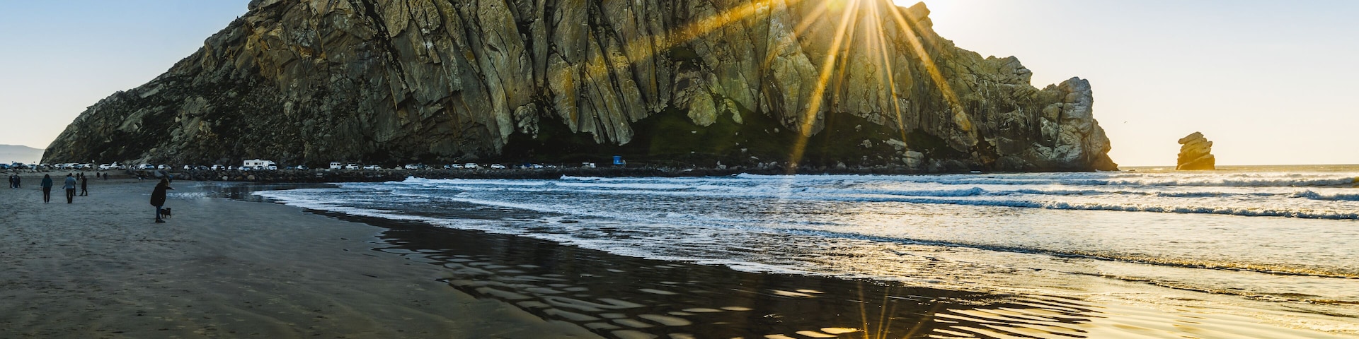Un acantilado rocoso frente al mar, con el sol brillando sobre la arena.