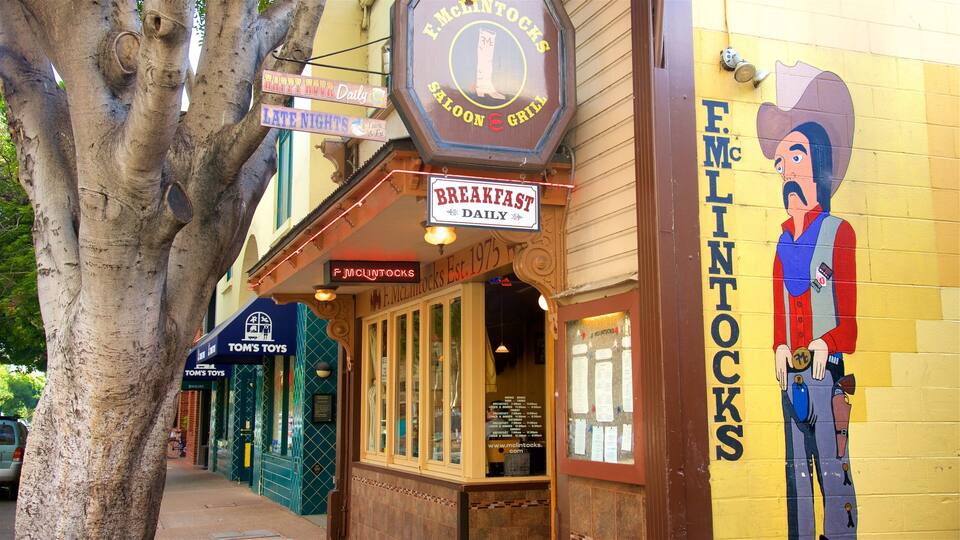 A storefront with a sign for F.McLintocks Saloon & Grill, a neon sign for Happy Hour, and a mural of a cowboy.