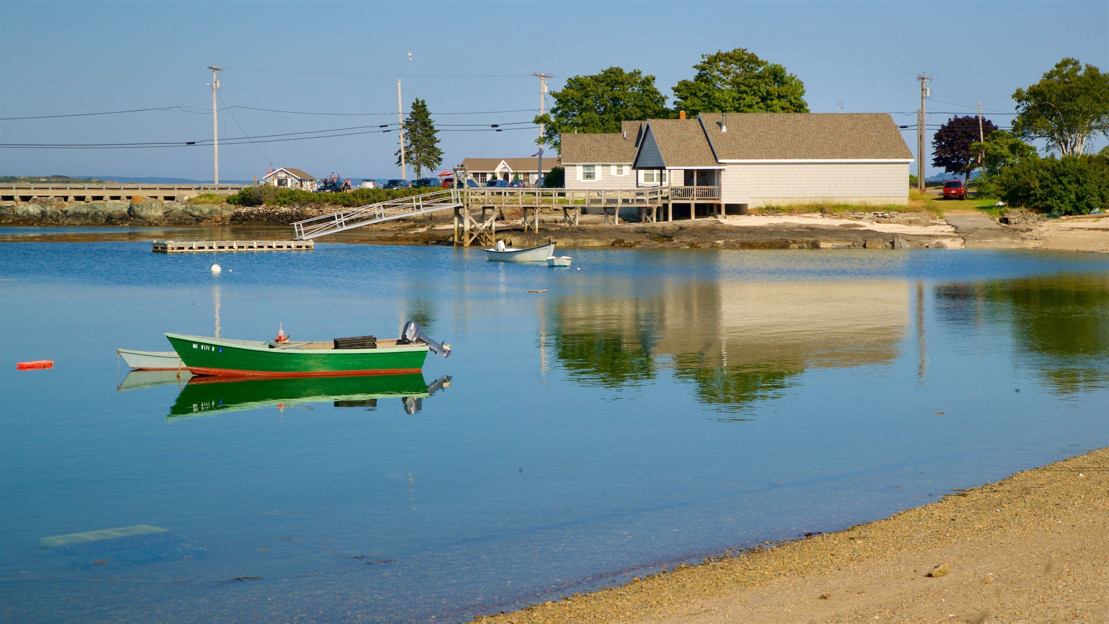 A calm lake with a green boat docked near the shore, a wooden pier, and a white house with a porch.
