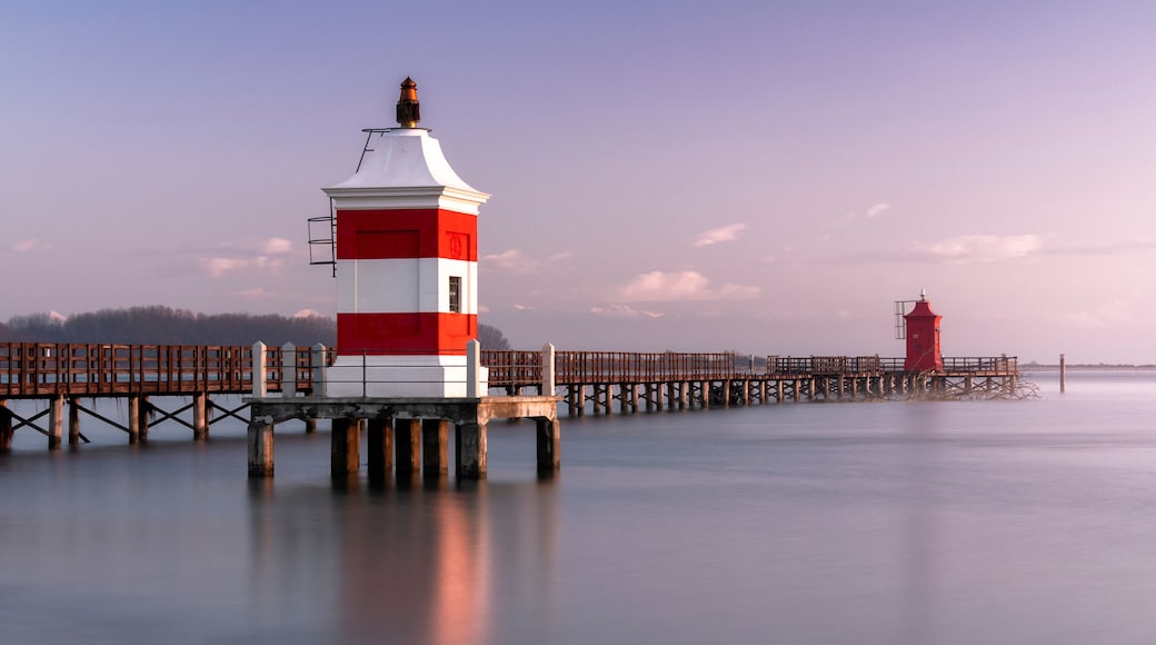 Long exposure shot of the Red Lighthouse of Lignano Sabbiadoro during a cold wintry sunrise. Calm water under a wooden boardwalk. Concept for relax and vacation