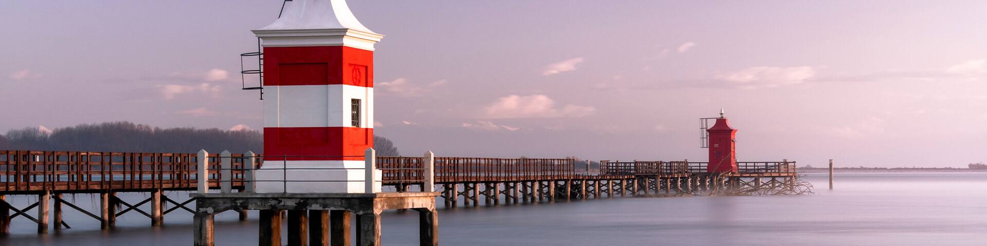 Long exposure shot of the Red Lighthouse of Lignano Sabbiadoro during a cold wintry sunrise. Calm water under a wooden boardwalk. Concept for relax and vacation