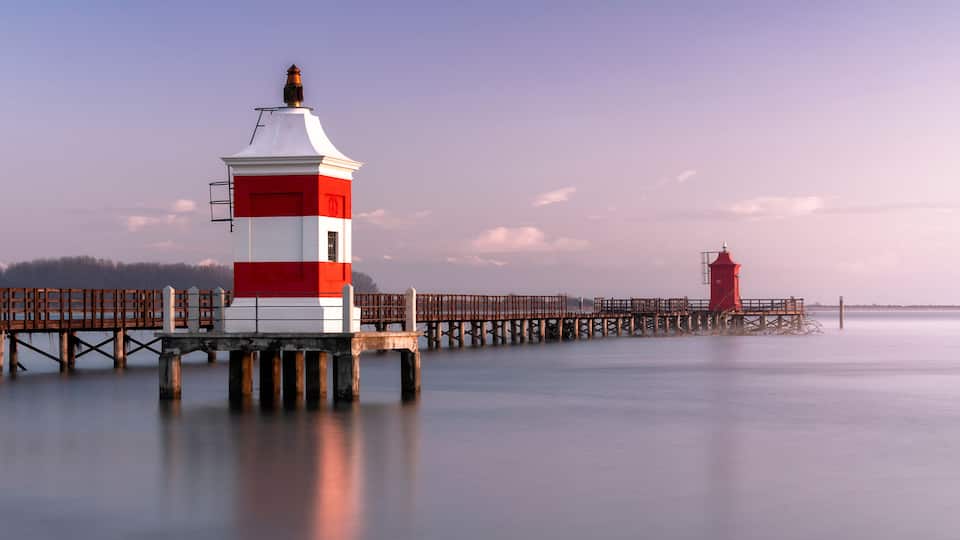 Long exposure shot of the Red Lighthouse of Lignano Sabbiadoro during a cold wintry sunrise. Calm water under a wooden boardwalk. Concept for relax and vacation