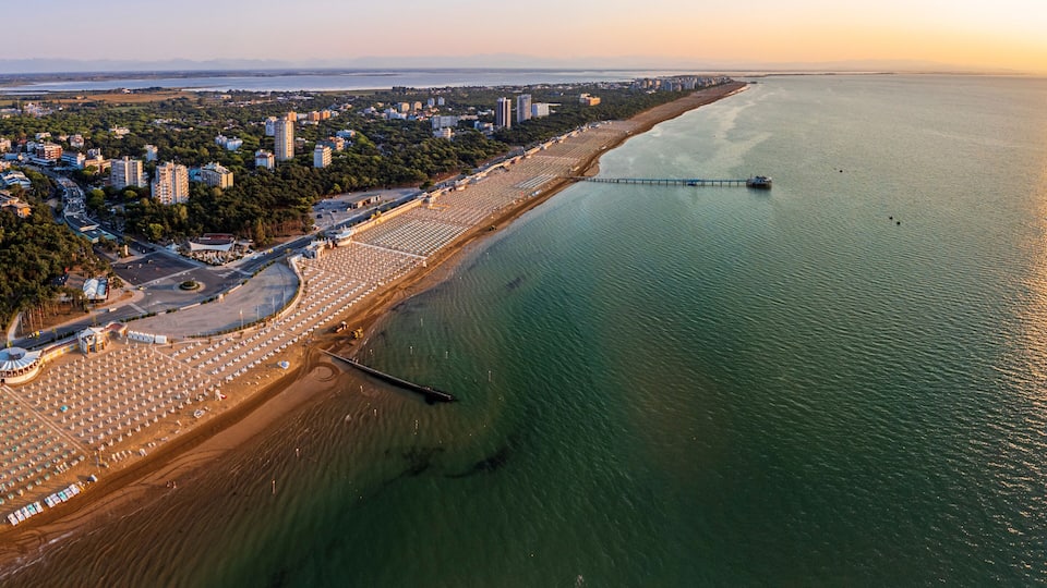 An aerial view of a coastal city with a long beach, a pier, and dense urban development.