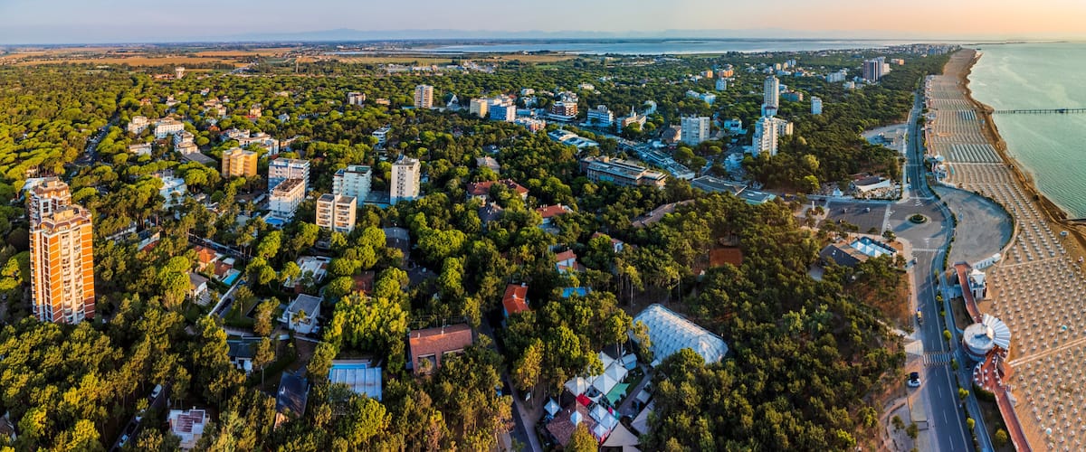 An aerial view of a coastal city with dense greenery, a beach with umbrellas, and a prominent bridge.