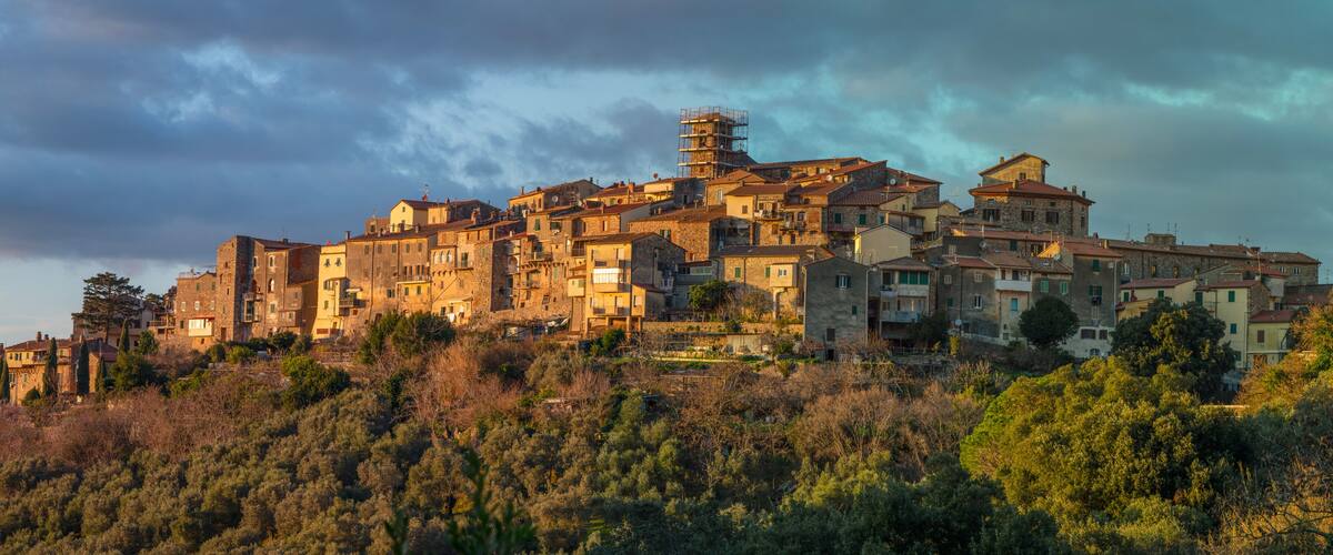 A hillside town with historic stone buildings, dense vegetation, and a cloudy sky.