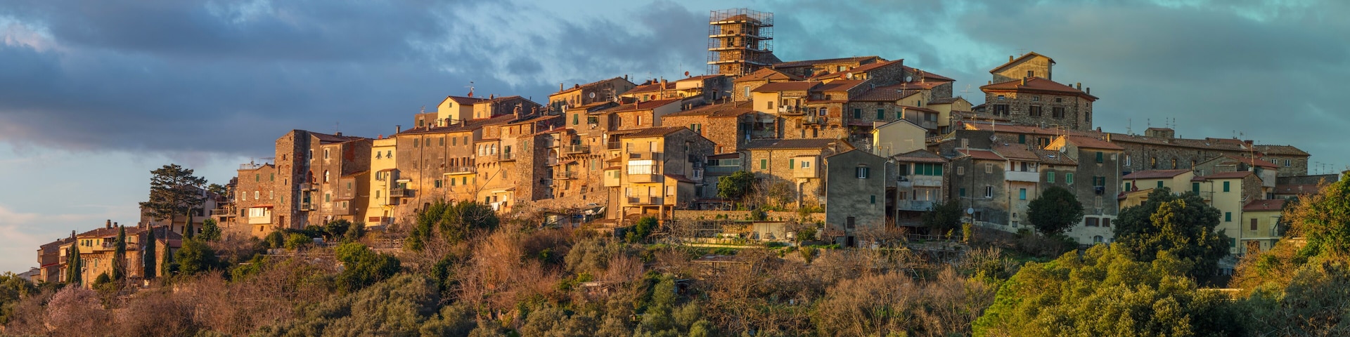 A hillside town with historic stone buildings, dense vegetation, and a cloudy sky.