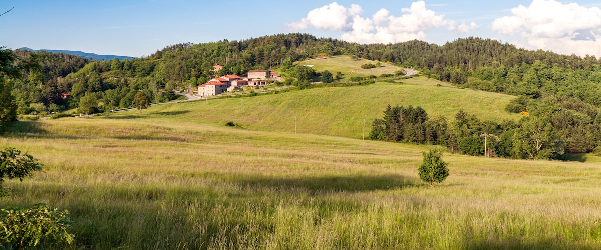 A rural landscape with rolling hills, a red-roofed building, and a clear blue sky.