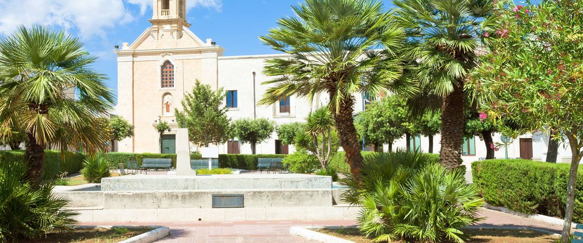 A church with a bell tower, surrounded by palm trees and a paved walkway.