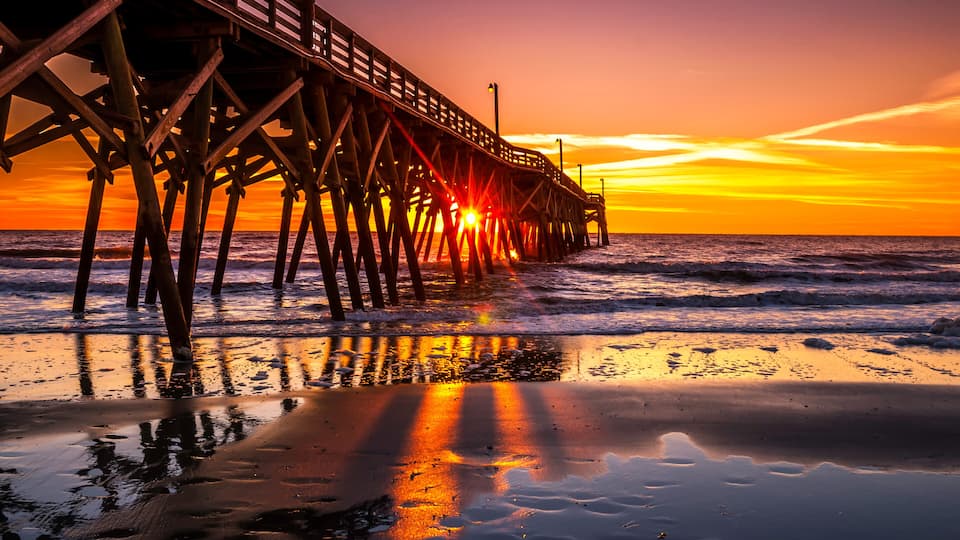 A pier extending into the ocean at sunset with the sun setting behind it.
