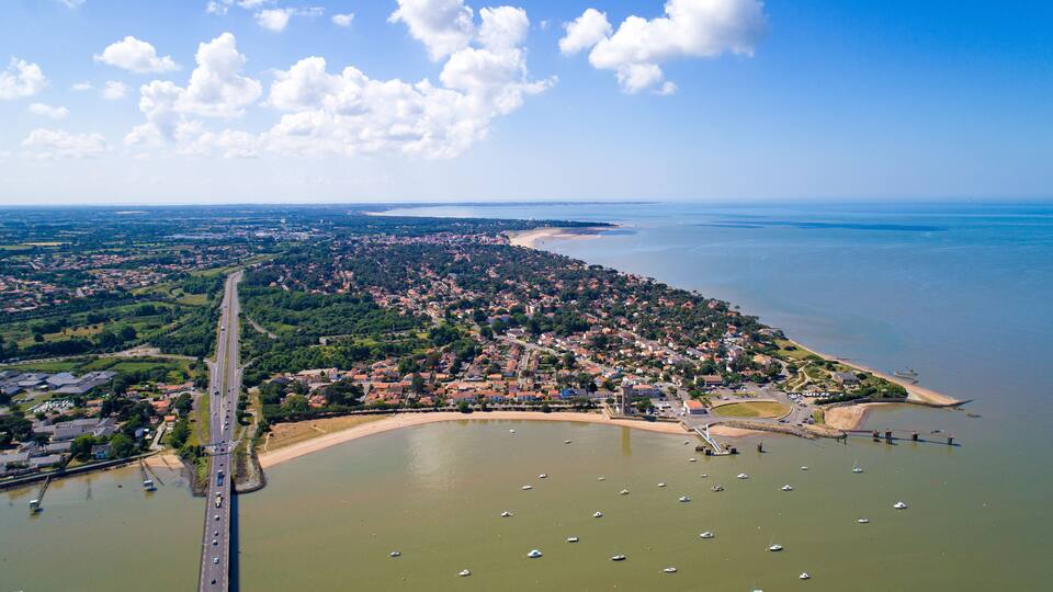 An aerial view of a coastal town with a bridge, marina, and surrounding greenery.