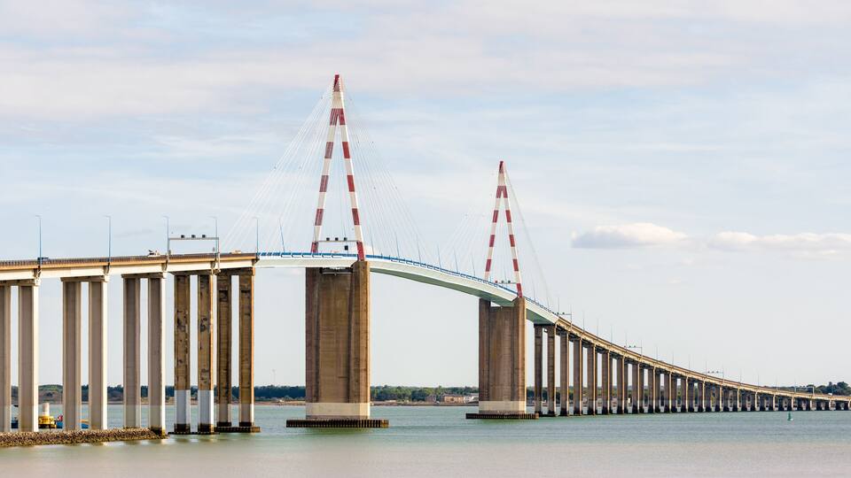 A long suspension bridge with tall pillars and red and white cables.