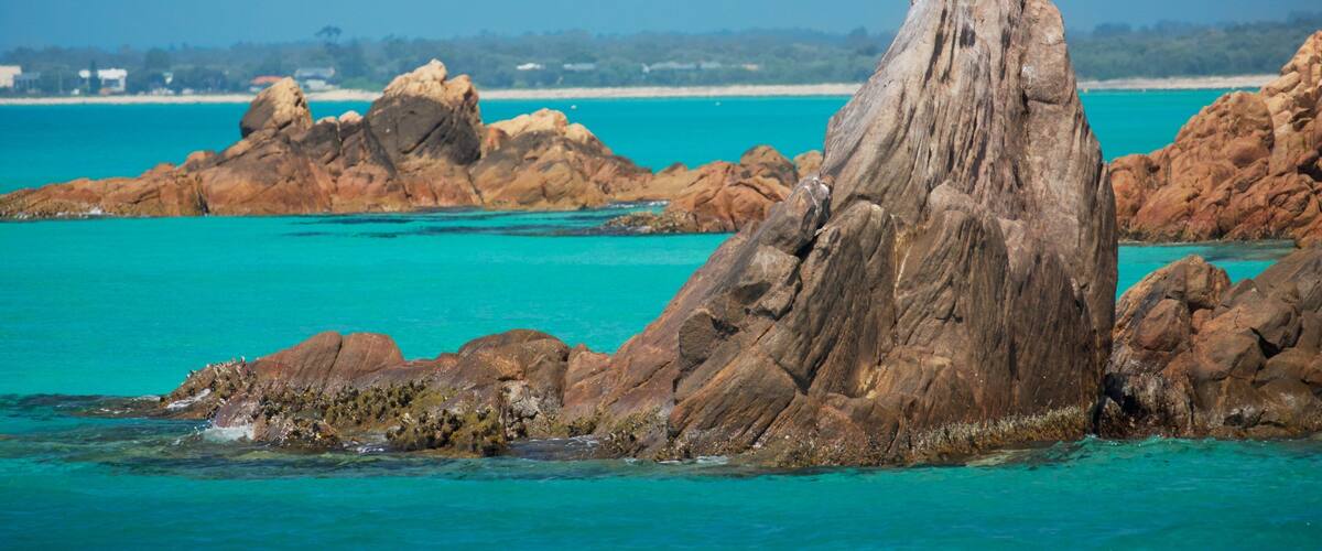 A rocky coastline with clear turquoise waters and a prominent rock formation in the foreground.
