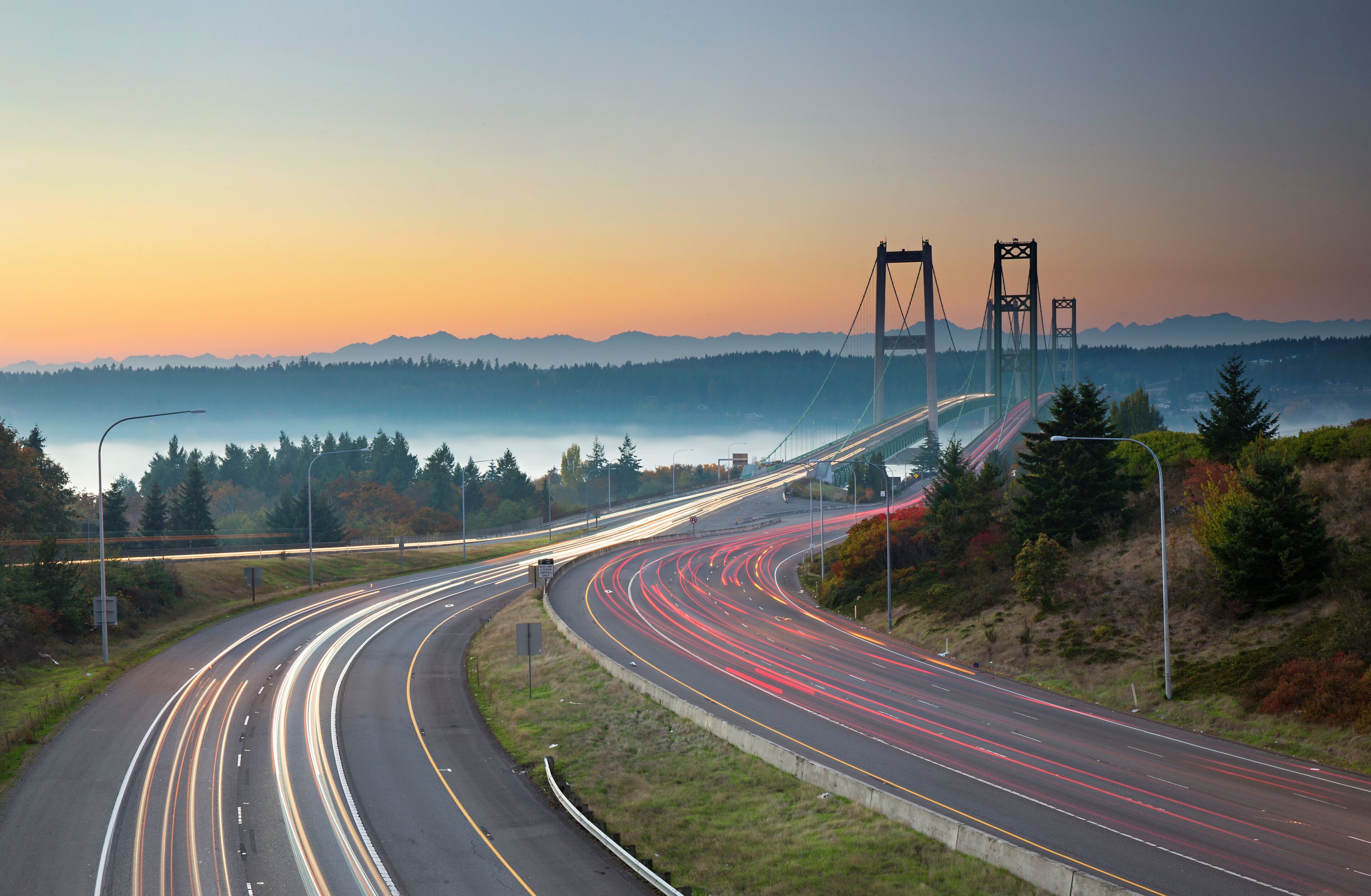 A multi-lane highway curving through a hilly landscape with a bridge in the distance.