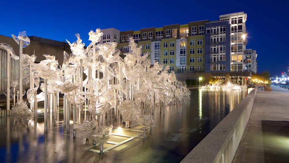 A nighttime cityscape with a reflective water feature and colorful buildings.