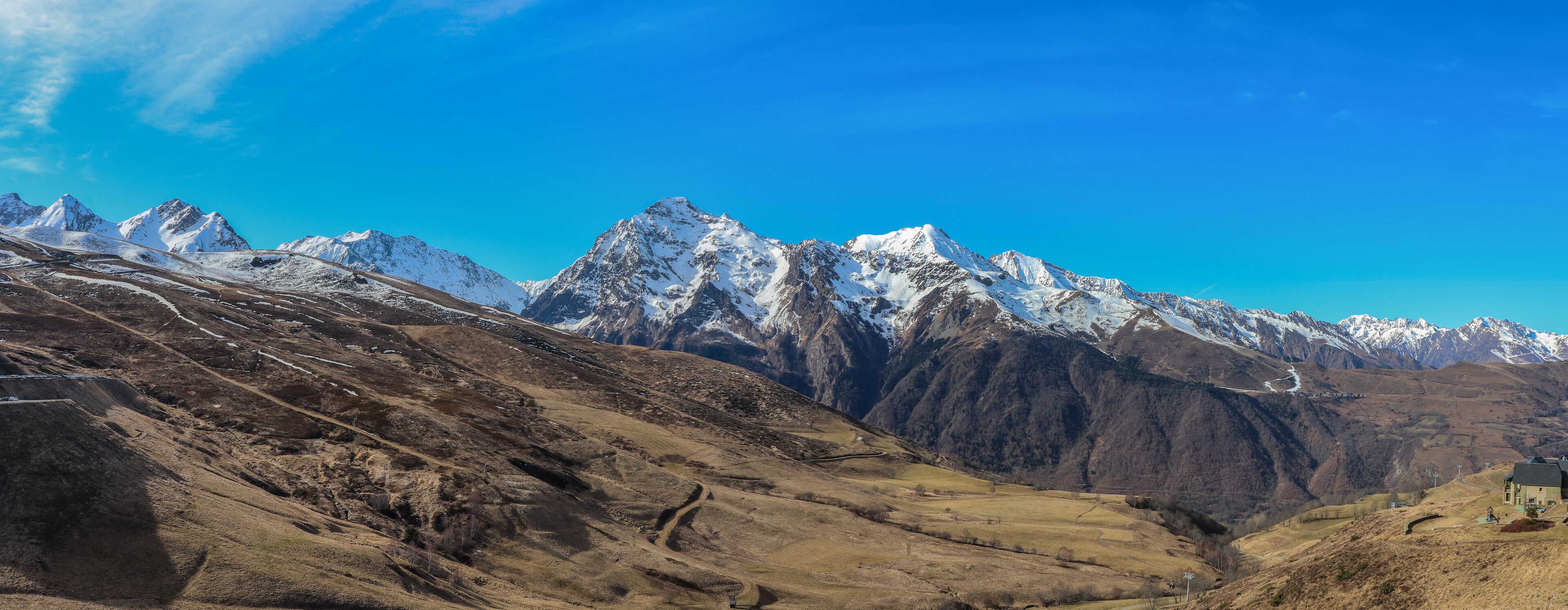 A mountainous landscape with snow-capped peaks, a winding road, and a small building in the valley.