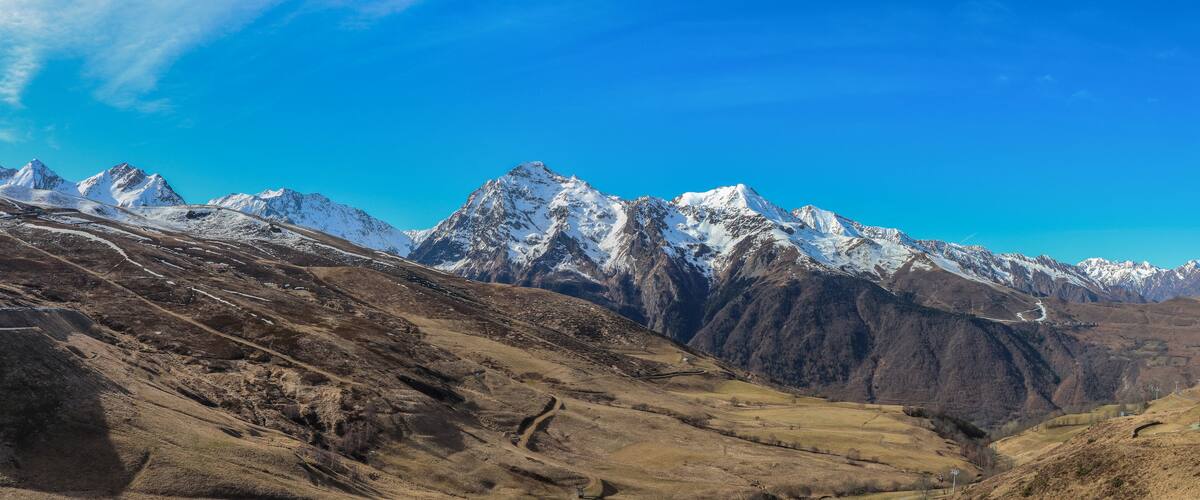 A mountainous landscape with snow-capped peaks, a winding road, and a small building in the valley.