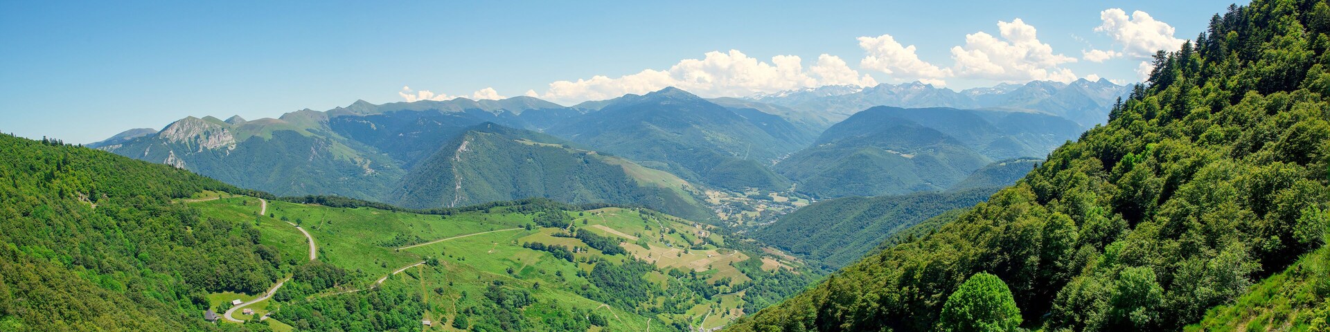 Paisagem montanhosa com vales verdejantes e um céu azul límpido.