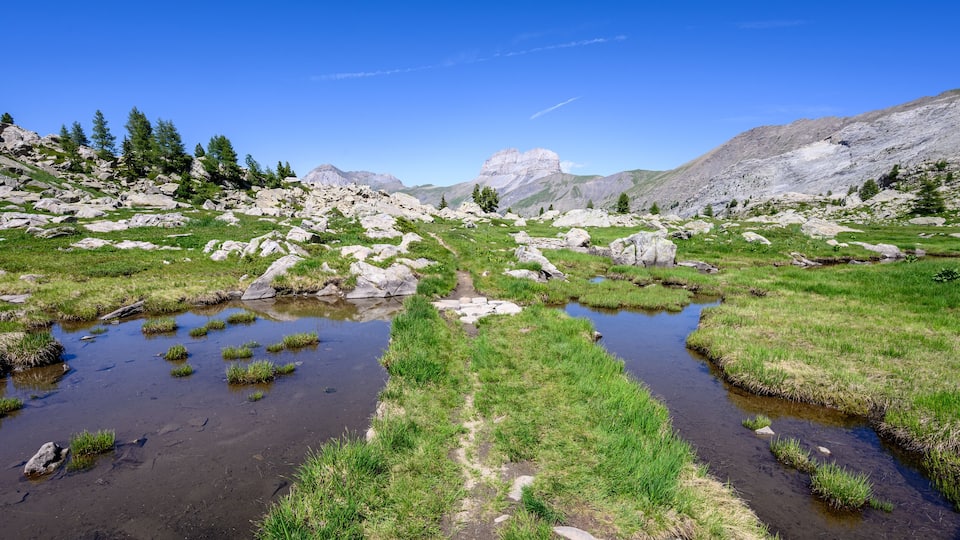 A mountainous landscape with rocky terrain, green grass, and a small stream.