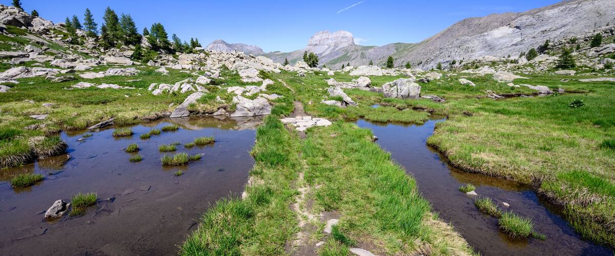 A mountainous landscape with rocky terrain, green grass, and a small stream.