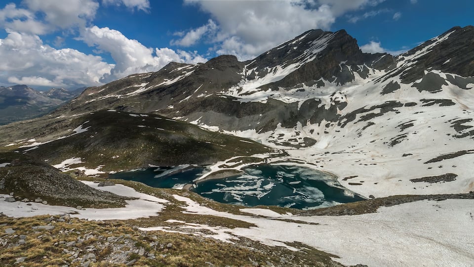 A mountain landscape with a lake and snow patches.