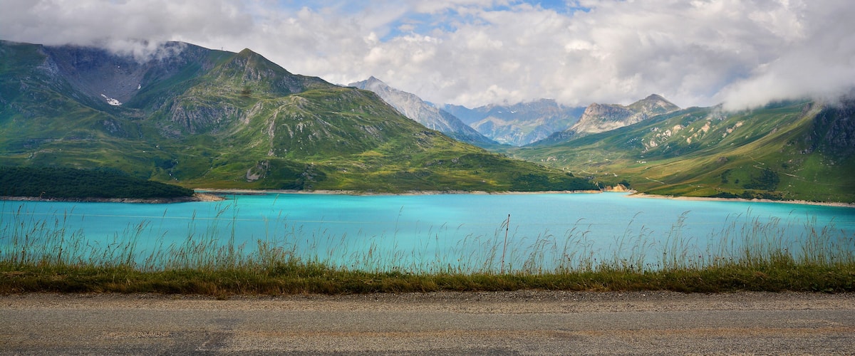 A turquoise lake surrounded by green mountains and a cloudy sky.
