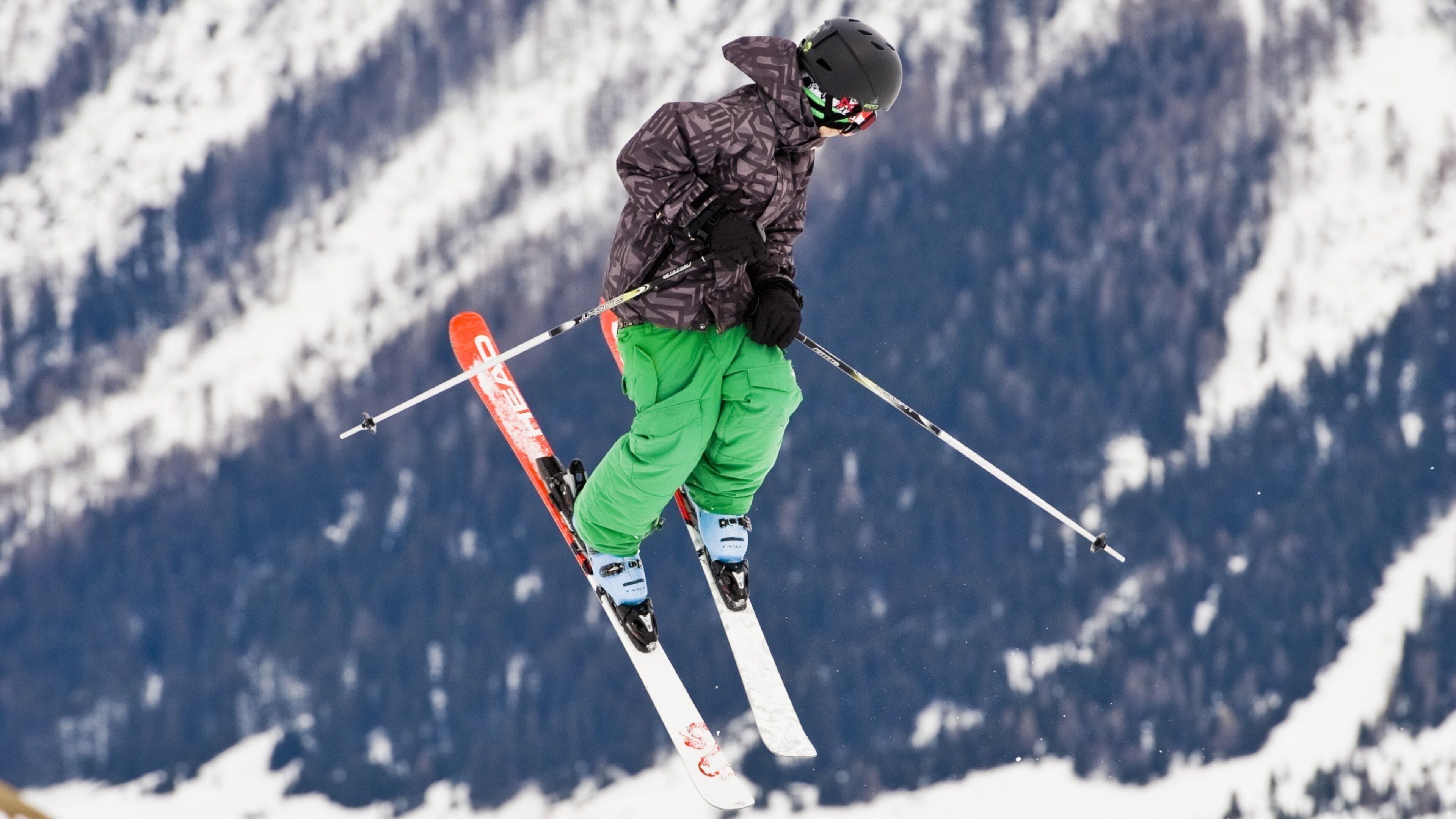 A skier in mid-air against a snowy mountain backdrop.