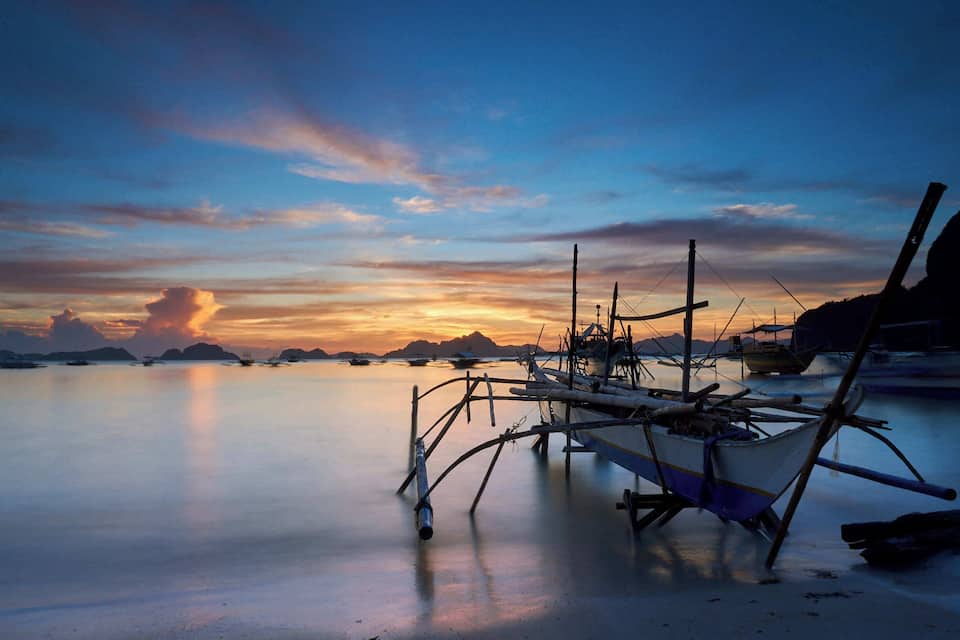 A calm coastal scene at sunset with boats and a clear sky.