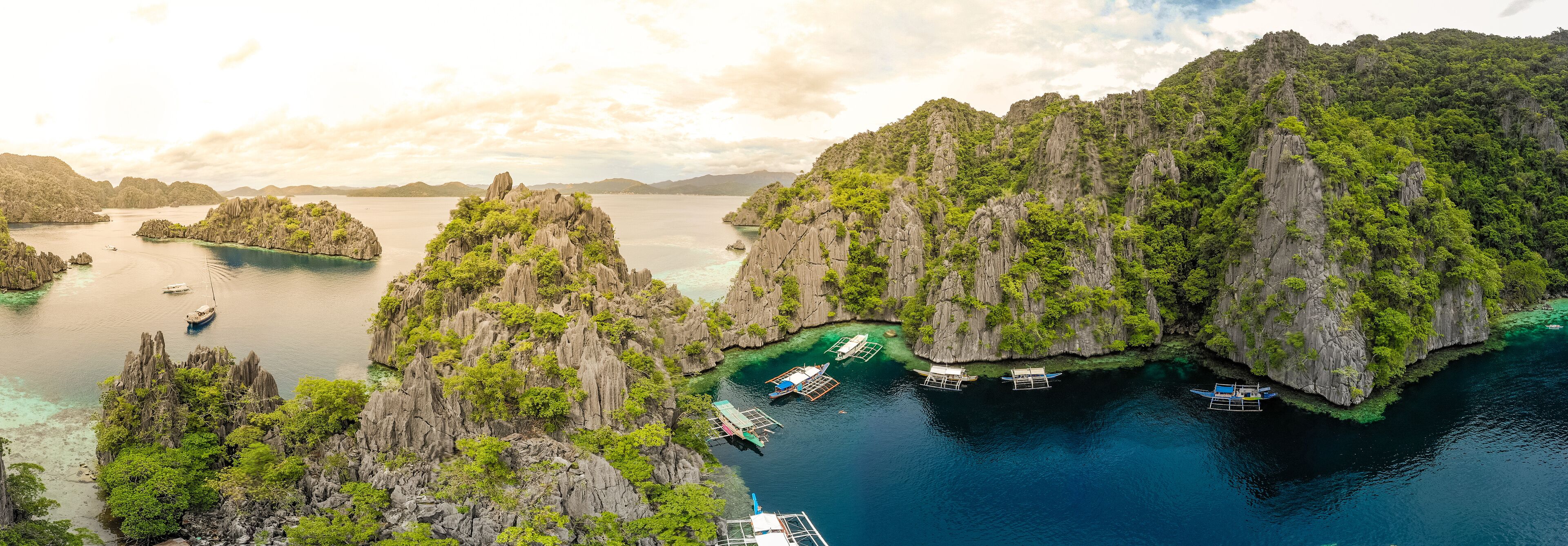 A coastal landscape with rocky cliffs, clear turquoise waters, and several boats anchored near the shore.