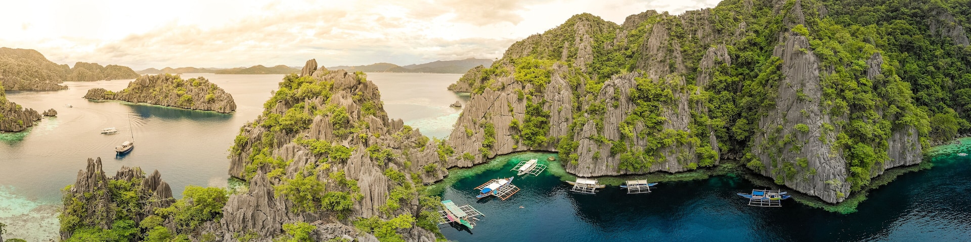 A coastal landscape with rocky cliffs, clear turquoise waters, and several boats anchored near the shore.