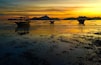 A sunset over a calm body of water with three boats anchored in the foreground.