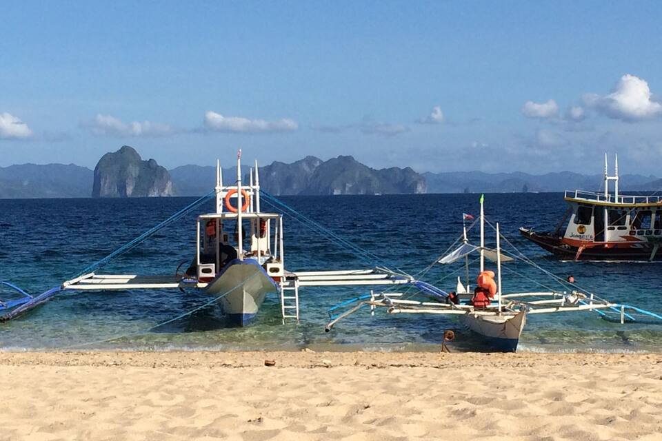 A beach with boats anchored in shallow water, clear skies, and distant mountains.