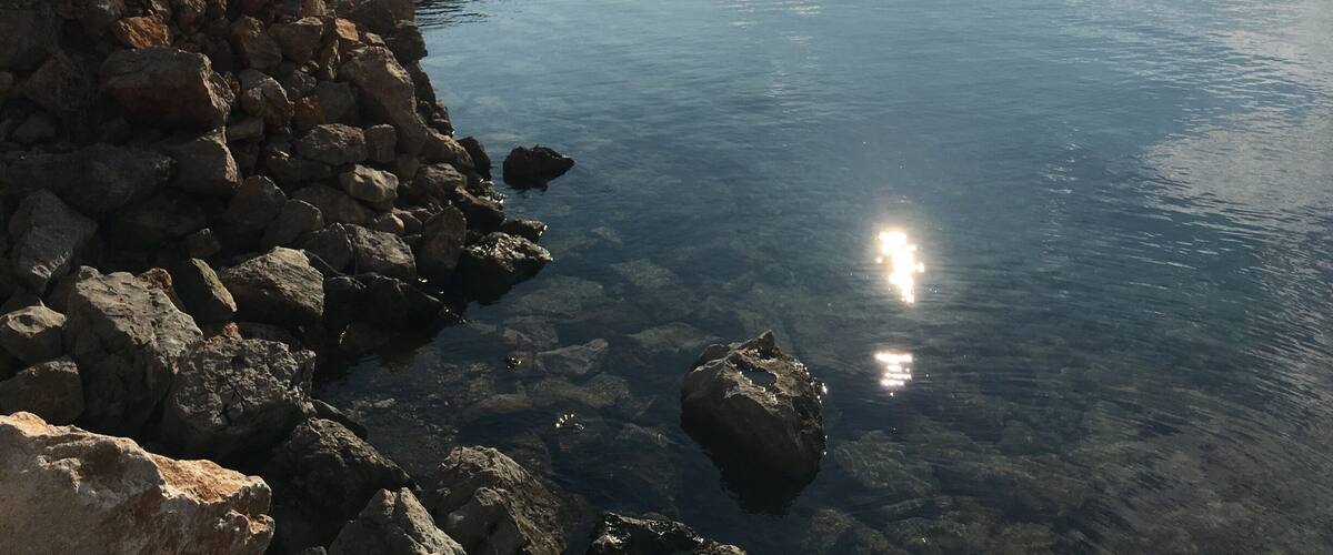 A rocky shoreline with calm water reflecting the sky.
