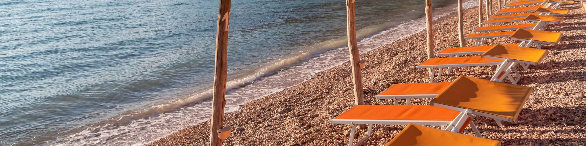 A beach with thatched umbrellas and orange lounge chairs.
