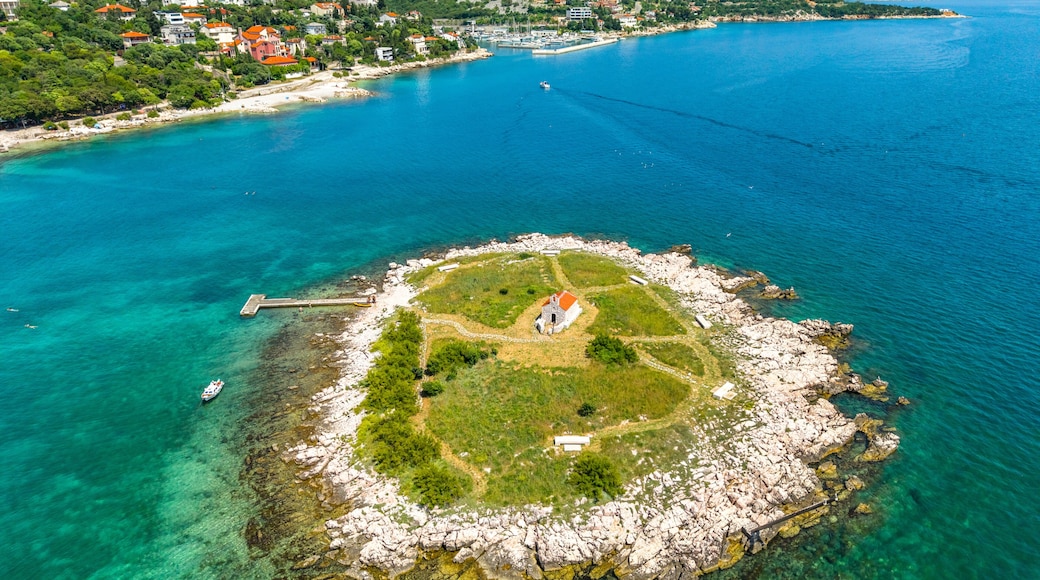 Drone image of a small rocky island San Marino near Novi Vinodolski, featuring a red-roofed chapel in the center, surrounded by green grass and crystal-clear turquoise waters