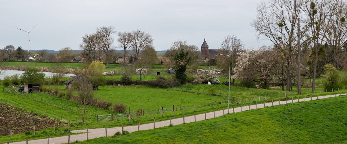 A rural landscape with a green field, a path, a windmill, and a church in the distance.