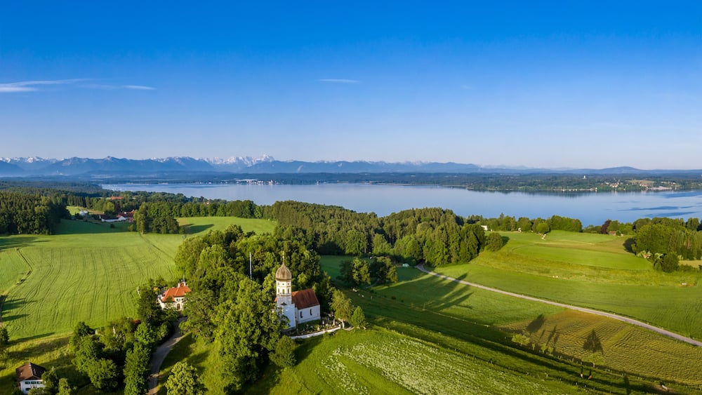 A lake surrounded by mountains, a church, and lush green fields.