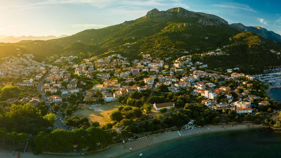 A coastal town with a mountain backdrop, a marina, and a beach.