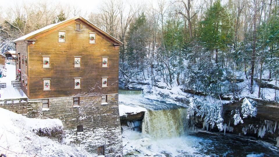 A wooden building with multiple windows, a waterfall, and a snowy forest.