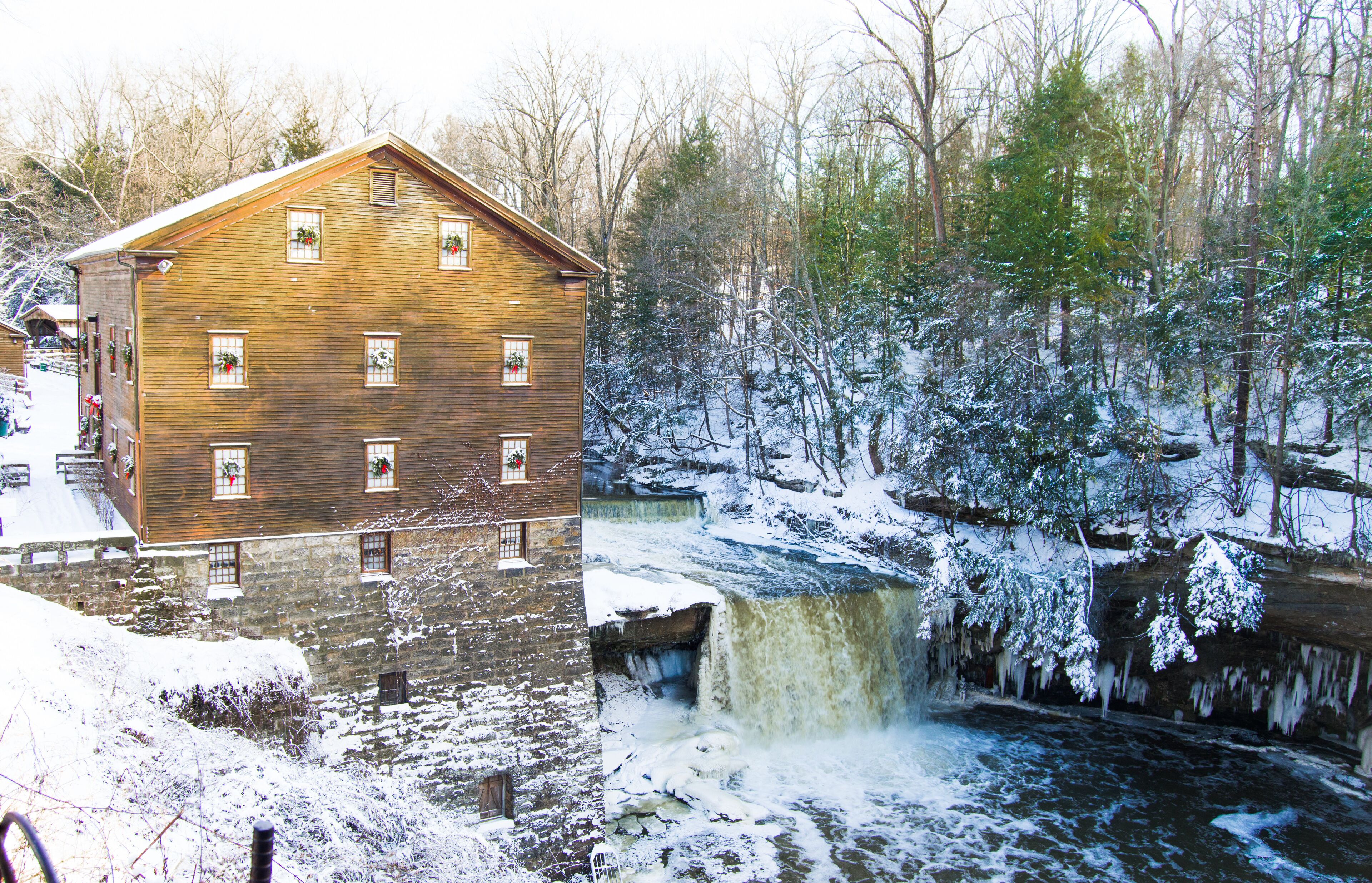 A wooden building with multiple windows, a waterfall, and a snowy forest.