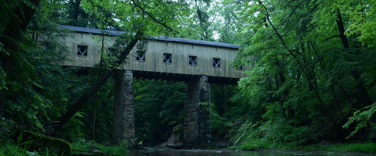 A wooden covered bridge over a river surrounded by lush greenery.