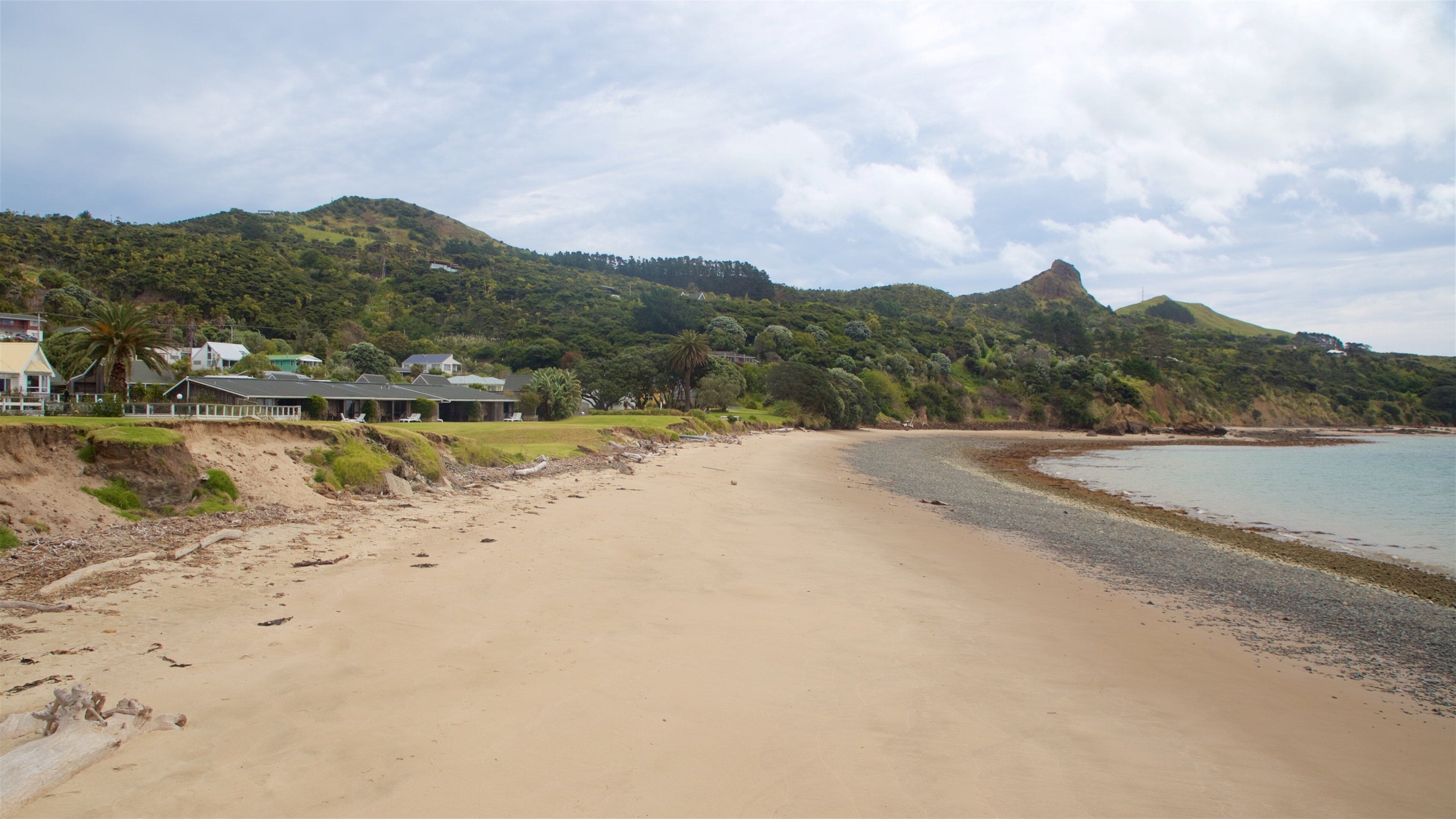 Una playa arenosa con colinas verdes exuberantes al fondo y un cielo despejado.