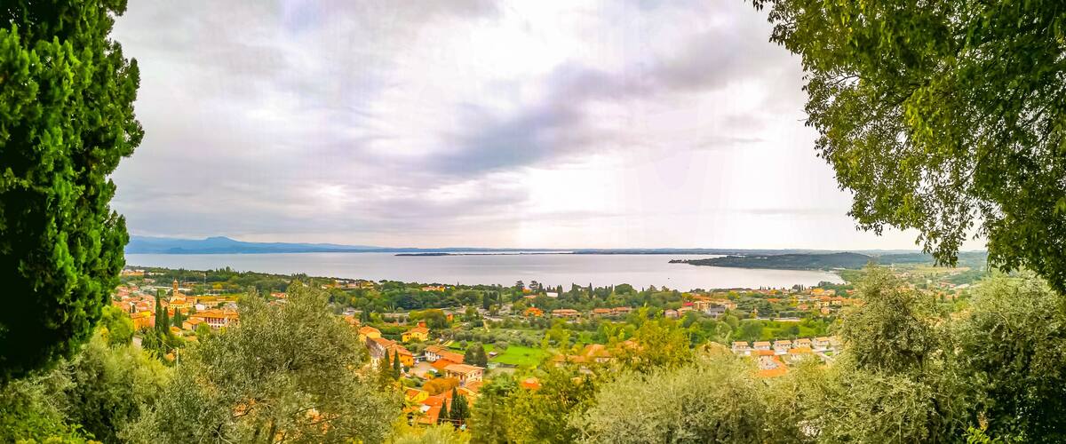 A coastal town with red-roofed buildings, surrounded by greenery and a large body of water.