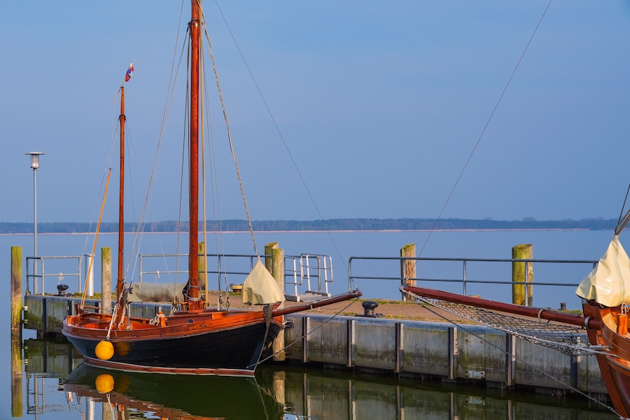 Un muelle con un barco amarrado, un poste de madera y una barandilla de metal.