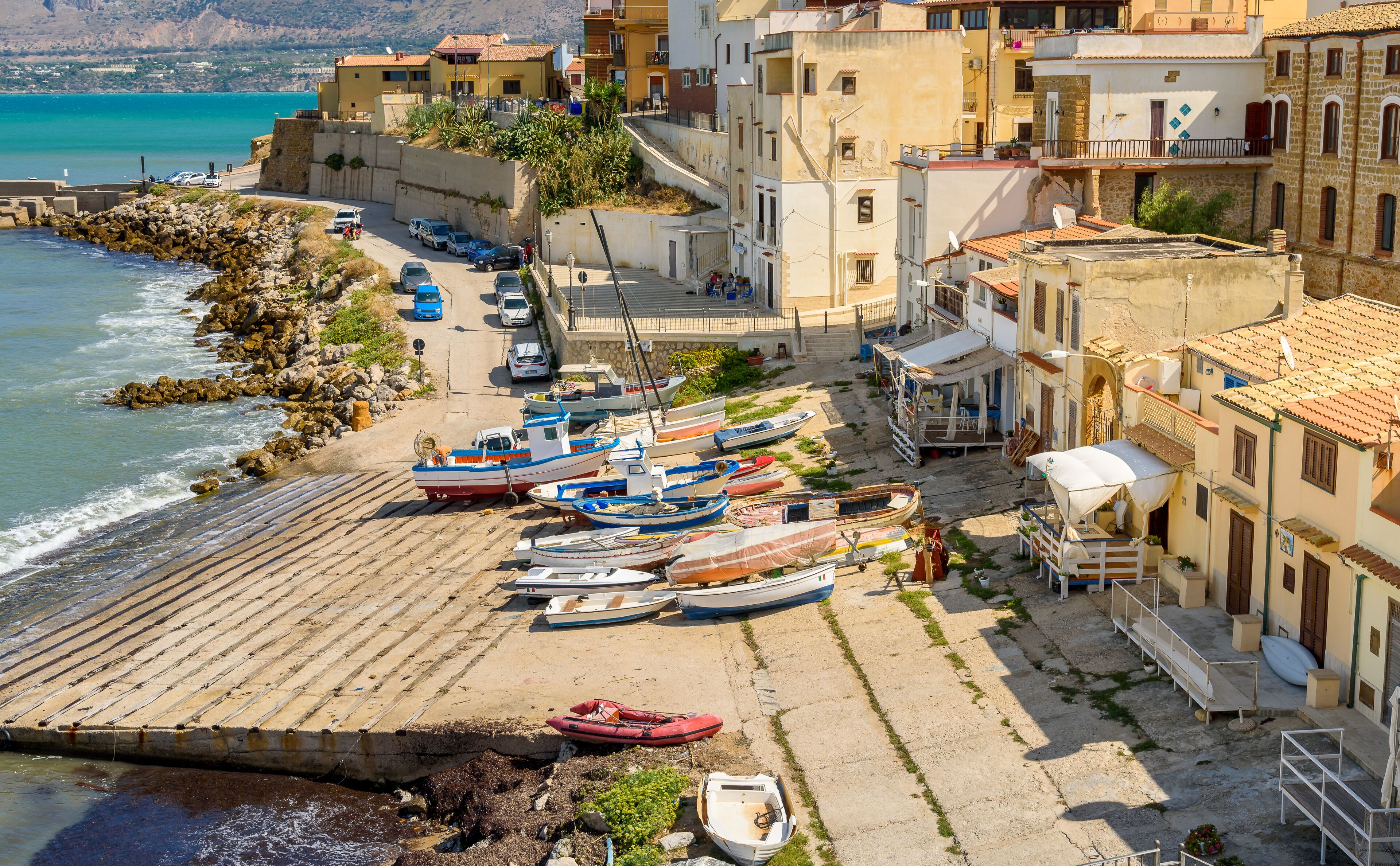 A coastal town with boats docked along the shore, buildings, and a rocky coastline.