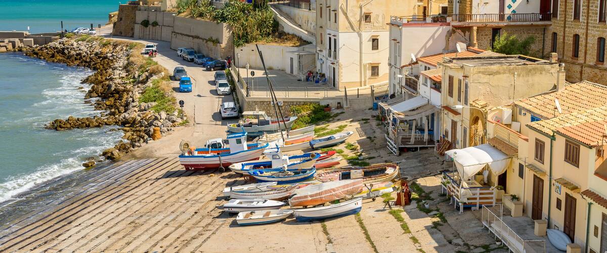 A coastal town with boats docked along the shore, buildings, and a rocky coastline.