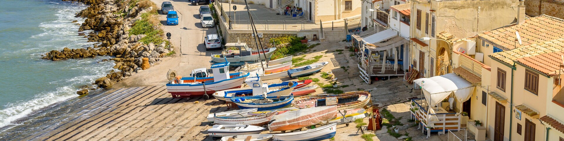 A coastal town with boats docked along the shore, buildings, and a rocky coastline.