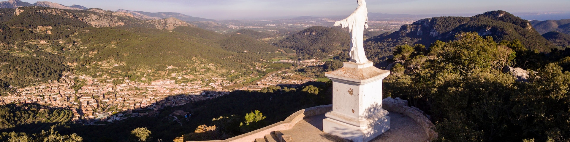 Eine Statue auf einem Hügel mit Blick auf eine Stadt und Berge.