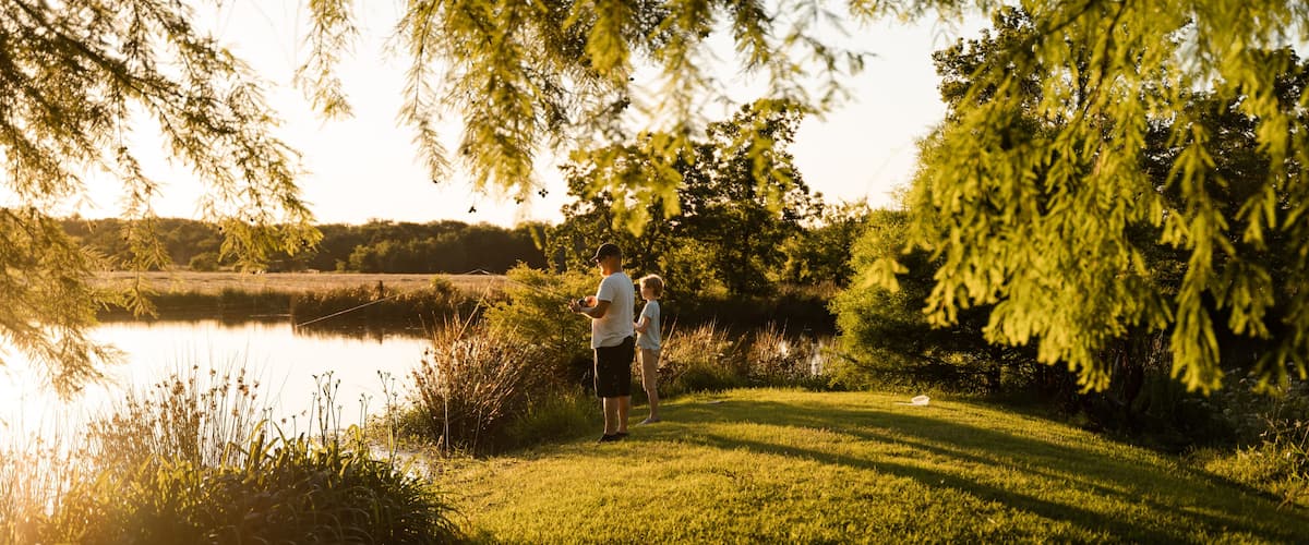 A person standing by a lake with trees and grass in the foreground.